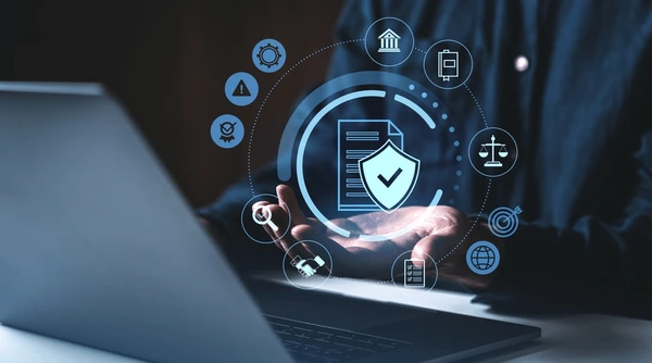 Holographic security icons surround a shielded document above a laptop, illustrating data protection and cybersecurity.